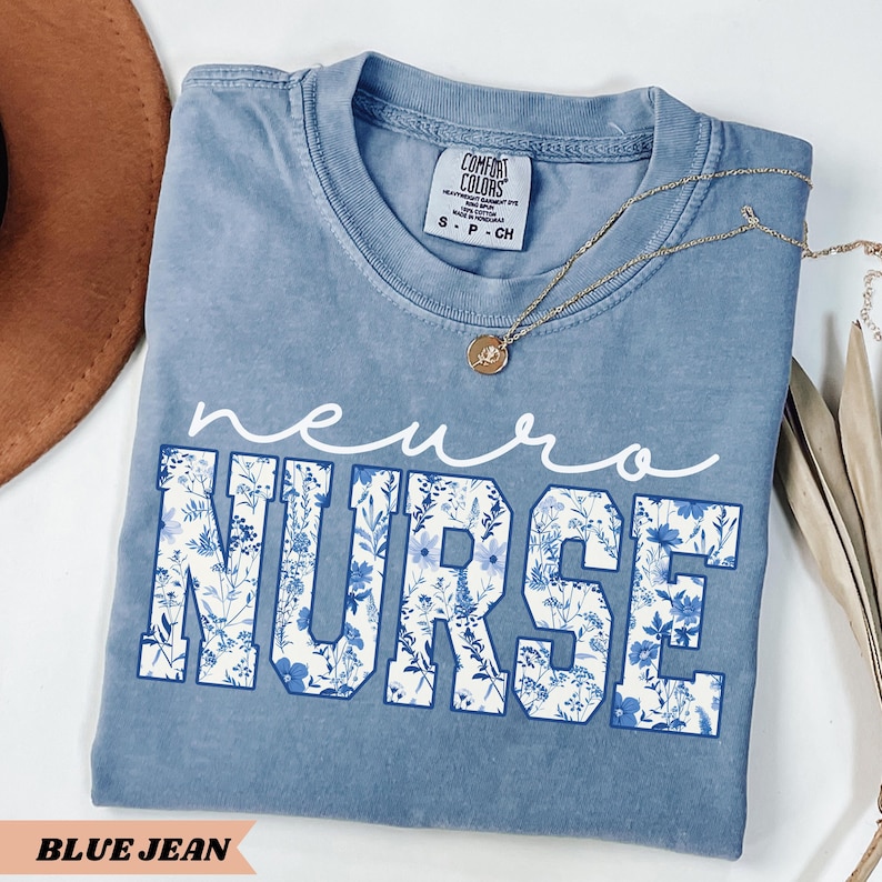 Puede incluir: Una camiseta azul vaquero con un dise&ntilde;o floral blanco que dice "neuro nurse".