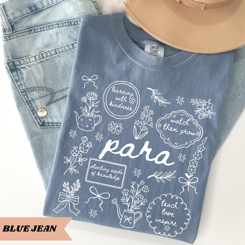 May include: A blue t-shirt featuring white line art of flowers, watering cans, and bows, with the text "para," "learning with kindness," "watch them grow," "planting seeds of knowledge," and "teach love inspire" printed on the front.