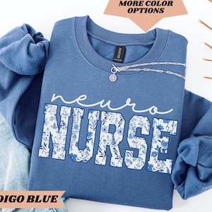 Puede incluir: Sudadera azul &iacute;ndigo con un dise&ntilde;o floral y el texto "neuro nurse" en blanco.