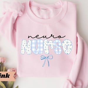 May include: A light pink sweatshirt with the words "neuro nurse" in black script and blue floral and gingham print. A blue bow graphic is below the word "nurse". The word "Pink" is in a pink banner in the lower left corner.