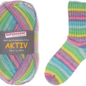 Pode incluir: Uma bola de fio multicolorido e uma meia a condizer. O fio é rotulado "SUPERGARNE AKTIV" e é uma mistura de rosa, azul, verde e amarelo. A meia tem riscas horizontais nas mesmas cores. O fio é 100 g / ca. 420 m.