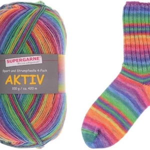 Puede incluir: Una madeja de hilo multicolor y un calcetín a juego. El hilo está etiquetado como "SUPERGARNE AKTIV" y es una mezcla de colores arcoíris. El calcetín también está a rayas con los mismos tonos vibrantes, ideal para tejer.