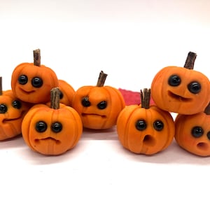 May include: A collection of small, orange pumpkins with expressive faces and dark eyes. Each pumpkin has a brown stem and varying facial expressions, creating a whimsical and playful Halloween theme.