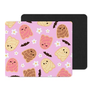 Puede incluir: Un mousepad rosa con un patr&oacute;n repetido de pan concha de dibujos animados, flores blancas y murci&eacute;lagos negros. Las conchas son en tonos de rosa, marr&oacute;n y amarillo. Una almohadilla rectangular negra est&aacute; detr&aacute;s de la almohadilla estampada.