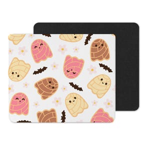 Puede incluir: Una alfombrilla de rat&oacute;n blanca con un patr&oacute;n repetido de pasteles de concha de dibujos animados en rosa, marr&oacute;n y amarillo, con peque&ntilde;as flores rosas y formas de murci&eacute;lago negras. La alfombrilla tiene un respaldo negro.