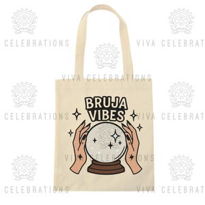 May include: Beige tote bag with the words "BRUJA VIBES" in black, along with a graphic of a crystal ball and hands. The design includes star accents. The bag has a simple, rectangular shape with a handle.