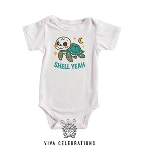 May include: White baby bodysuit with a cartoon turtle design. The turtle has a skull-like face, a teal shell, and orange and yellow accents. The text "SHELL YEAH" is printed below the turtle in teal.