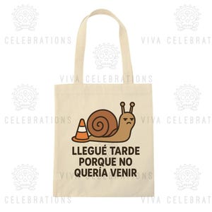 May include: Beige tote bag featuring a cartoon snail with a traffic cone and the text "Llegué tarde porque no quería venir". The snail is brown with a grumpy expression. The bag has two handles.