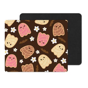 Puede incluir: Una alfombrilla de rat&oacute;n rectangular con un fondo marr&oacute;n que presenta un patr&oacute;n de pasteles de concha de dibujos animados en rosa, beige y marr&oacute;n, junto con flores blancas. Una alfombrilla de rat&oacute;n negra est&aacute; detr&aacute;s.