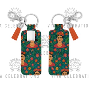 May include: Two Frida Kahlo-themed hand sanitizer holders with keychains. The teal holders feature a floral pattern and portraits of Frida Kahlo. Each holder has a silver keychain and an orange tassel. The text "VIVA CELEBRATIONS" is printed on the background.