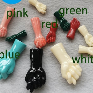 Op de afbeelding: Assortiment van tien kleine plastic handen in verschillende kleuren, waaronder roze, rood, groen, blauw, wit en zwart. De handen zijn allemaal in een vuist.