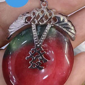 May include: A red and green jade pendant with a silver filigree design. The pendant features a Chinese character in the center.