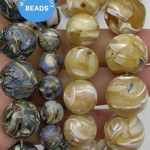 May include: Two strands of round iridescent shell beads. One strand is a mix of blue, green, and brown colors. The other strand is a mix of white and yellow colors. The beads are strung on a clear elastic cord. The beads are labeled "WK DIY Jewelry Beads".