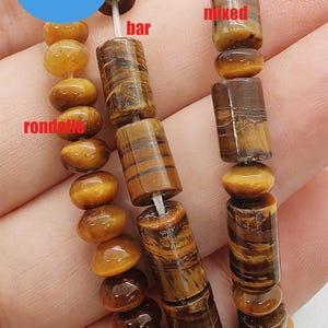 May include: Close-up of three strands of beads. One strand features small, round, amber-colored beads. The other two strands have a mix of amber-colored and brown, cylindrical beads. The beads are strung on a white cord. The image includes a blue circle with the text "WK DIY Jewelry BEADS".