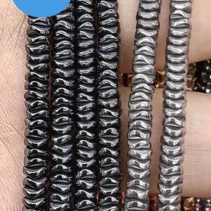 Pode incluir: Um close-up de um fio de contas de hematita preta. As contas são facetadas e têm um acabamento brilhante. As contas são enfiadas em um cordão e estão prontas para serem usadas para fazer joias.