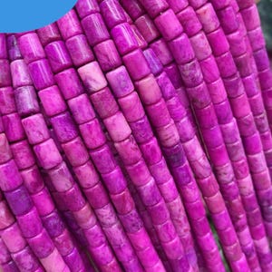 May include: Multiple strands of cylindrical, vibrant magenta-colored beads with a marbled texture. The beads are arranged in vertical rows, showcasing a consistent shape and size. A blue circular graphic in the upper left corner displays the text JEWERLY ADS.