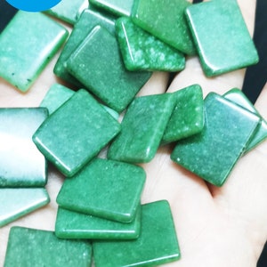 Op de afbeelding: Een verzameling groene vierkante edelsteen kralen. De kralen zijn glad en hebben een licht doorschijnende uitstraling. De kralen zijn op een hand in een stapel gelegd.