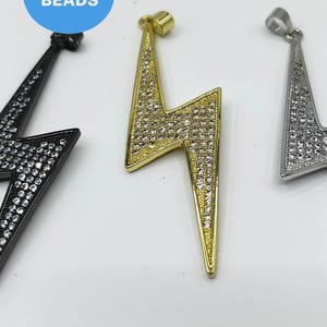 May include: Three silver, gold, and black lightning bolt pendants with clear rhinestones. The pendants are all the same shape and size, but they are different colors.