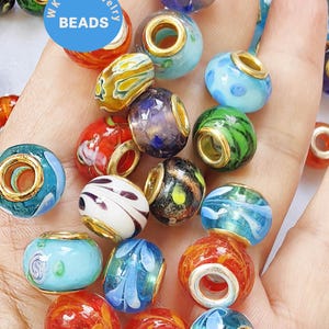 May include: A selection of vibrant glass beads with gold-coloured metal accents. The beads display diverse patterns, such as swirls, dots, and floral motifs, in hues of blue, red, green, and yellow. The image includes a blue circle with the text "WK DIY Jewelry BEADS."