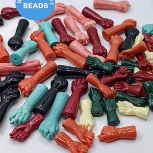 Könnte beinhalten: Eine große Sammlung von bunten, handförmigen Perlen aus Kunststoff. Die Perlen sind in verschiedenen Farben, darunter Rot, Orange, Gelb, Grün, Blau und Lila. Die Perlen haben alle die Form einer Hand mit einer geschlossenen Faust.