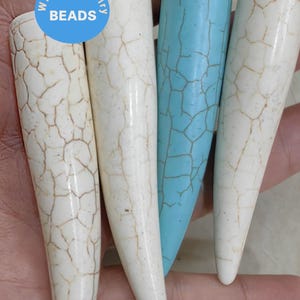 Puede incluir: Cuatro cuentas largas y puntiagudas, blancas y turquesa, con un patrón agrietado. Las cuentas se sostienen en una mano. Las cuentas están etiquetadas como "WK DIY Jewelry Beads".