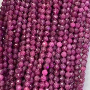 Könnte beinhalten: Eine Strähne rosafarbener facettierter Edelsteinperlen. Die Perlen sind rund und haben eine glatte, polierte Oberfläche.