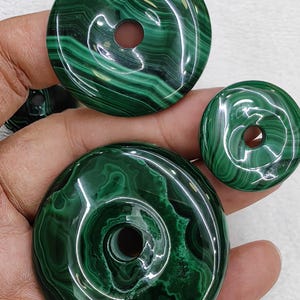 以下が含まれることがあります： 中央に穴が開いた緑色のマラカイト製のドーナツビーズが3つ。ビーズはサイズが異なり、磨かれた光沢のある仕上げになっています。