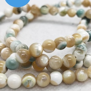 Può includere: Fili di perline rotonde e iridescenti nei toni crema, beige e verde acqua. Le perline sono infilate insieme, creando un motivo fluido. Queste perline sono adatte per la creazione di gioielli.