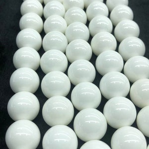 May include: A strand of white ceramic beads, each bead is round and smooth. The beads are arranged in rows, creating a uniform and symmetrical pattern.