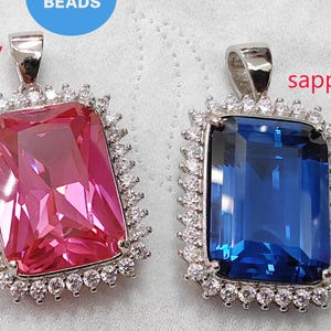 May include: Two silver pendants with clear crystal settings. The pendant on the left has a pink gemstone and the text "ruby". The pendant on the right has a blue gemstone and the text "sapphire".