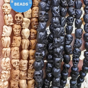 May include: A close-up of two strands of skull-shaped beads. One strand is made of natural bone-coloured beads, and the other strand is made of black beads. The beads are all carved with detailed skull faces. The text "WK DIY Jewelry Beads" is visible on a blue sticker.