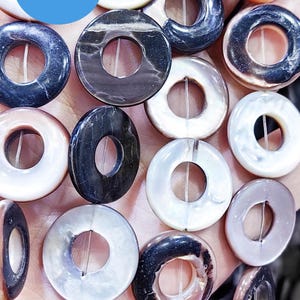 May include: A collection of round, donut-shaped beads in various colors, including white, black, and iridescent hues. The beads have a hole in the center and are strung together. The image includes a blue circle with the text "WK DIY Jewelry BEADS".