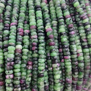 Puede incluir: Una hebra de cuentas de piedras preciosas verdes y rosas. Las cuentas son redondas y tienen un acabado liso y pulido.