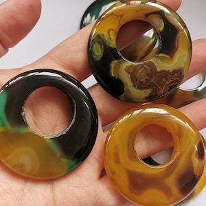 May include: Three agate stone rings with a hole in the center. The rings are yellow, green, and black with brown swirls.