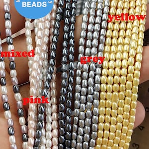 Könnte beinhalten: Nahaufnahme von Perlensträngen in verschiedenen Farben, darunter Weiß, Rosa, Schwarz, Grau und Gelb. Die Perlen sind in Reihen angeordnet und haben einen Durchmesser von etwa 6 mm. Das Bild enthält ein Lineal zur Skalierung.