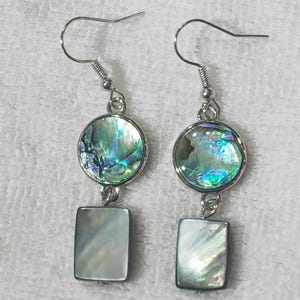 May include: Dangle earrings featuring iridescent abalone shell and rectangular mother-of-pearl drops. The earrings have silver-tone hooks and circular settings. The abalone shells show green, blue, and purple hues.