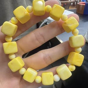 May include: A yellow bracelet made of square-shaped beads. The bracelet is made of a smooth, polished material.