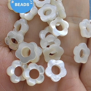 May include: A collection of white, flower-shaped beads with a hole in the center. The beads are made of mother of pearl and have a slightly iridescent sheen.