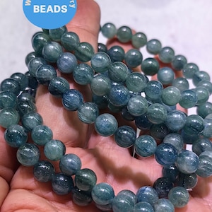 May include: A close-up of a stack of blue and green gemstone bracelets. The bracelets are made of round beads and have a smooth, polished finish. The beads have a subtle shimmer and a striated pattern.
