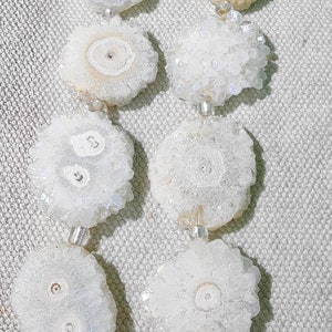 May include: A strand of white crystal beads with an iridescent sheen. The beads are round and have a flower-like pattern. The beads are strung on a silver wire.