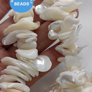 Puede incluir: Una hebra de cuentas de concha blanca iridiscente. Las cuentas son de forma irregular y tienen un aspecto natural y orgánico. Las cuentas están enhebradas en un hilo transparente y están listas para ser utilizadas para la elaboración de joyas.