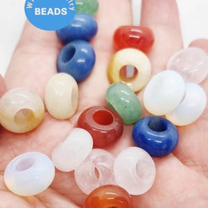 Könnte beinhalten: Eine Sammlung farbenfroher Perlen in verschiedenen Formen und Größen, darunter runde, ovale und donut-förmige. Die Perlen sind in den Farbtönen Rot, Blau, Grün, Weiß und Orange gehalten. Das Bild enthält den Text "WK DIY Jewelry BEADS" in einem blauen Kreis.