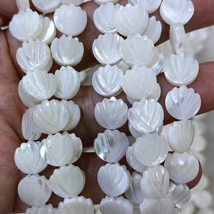 Könnte beinhalten: Eine Strähne aus weißen Perlmuttkugeln mit einem geschnitzten Blumendesign. Die Perlen sind auf einer durchsichtigen Gummikordel aufgefädelt.