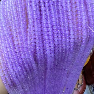 May include: A strand of light purple beads, made of smooth, round, translucent stones. The beads are strung together on a thin, white thread.