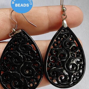 Può includere: Un paio di orecchini pendenti in filigrana nera con ganci argentati. Gli orecchini hanno la forma di una lacrima e un design delicato e intricato.