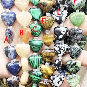 May include: Strands of heart-shaped gemstone beads in various colors and patterns. The beads include blue sodalite, yellow jasper, green malachite, tiger's eye, and black and white patterned stones. Each bead is strung with a clear spacer.