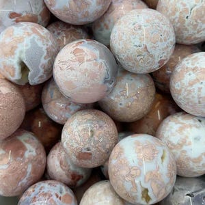 May include: A collection of polished stone spheres in shades of pink, white, and brown. The spheres have a marbled appearance with intricate patterns and variations in color. The spheres are likely decorative items or collectibles.