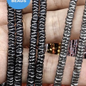 May include: A close-up of four strands of black hematite beads. The beads are faceted and have a shiny finish. The beads are strung on a clear elastic cord. The beads are approximately 6mm in diameter.  WK DIY Jewelry Beads.