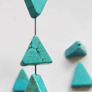 Puede incluir: Cuentas de color turquesa con forma de triángulo enhebradas en un alambre. Las cuentas tienen un aspecto moteado y veteado.