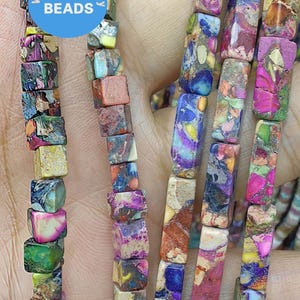 May include: Multicolored square beads made of jasper, a type of gemstone. The beads are strung on a string and are ready to be used for jewelry making.